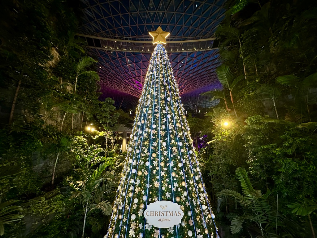 Giant Christmas tree, flanked by greenery, at entrance to vortex waterfall in JEWEL Changi Airport.